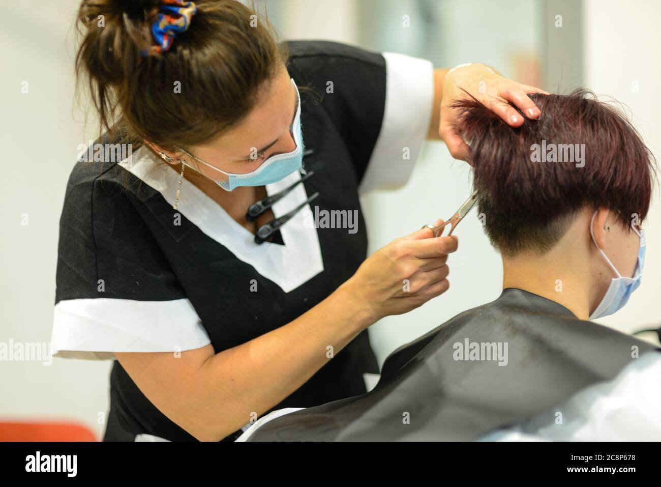 Hair stylist wearing face mask cutting and styling the hair of a dark ...