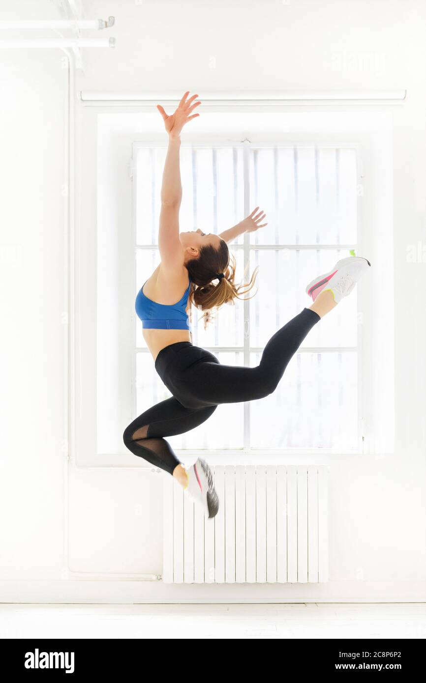 Woman doing a graceful acro gymnastic butterfly jump with outstretched arms in a high key gym in a health and fitness or active lifestyle concept Stock Photo