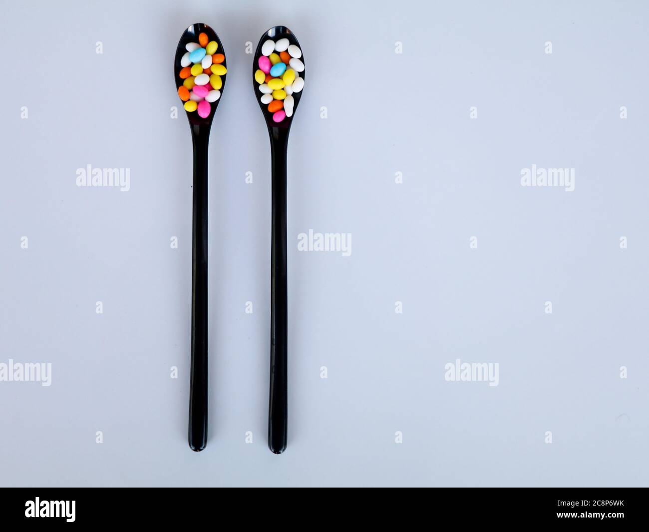 Multi colored sweet fennel sugar candy in black spoons against white