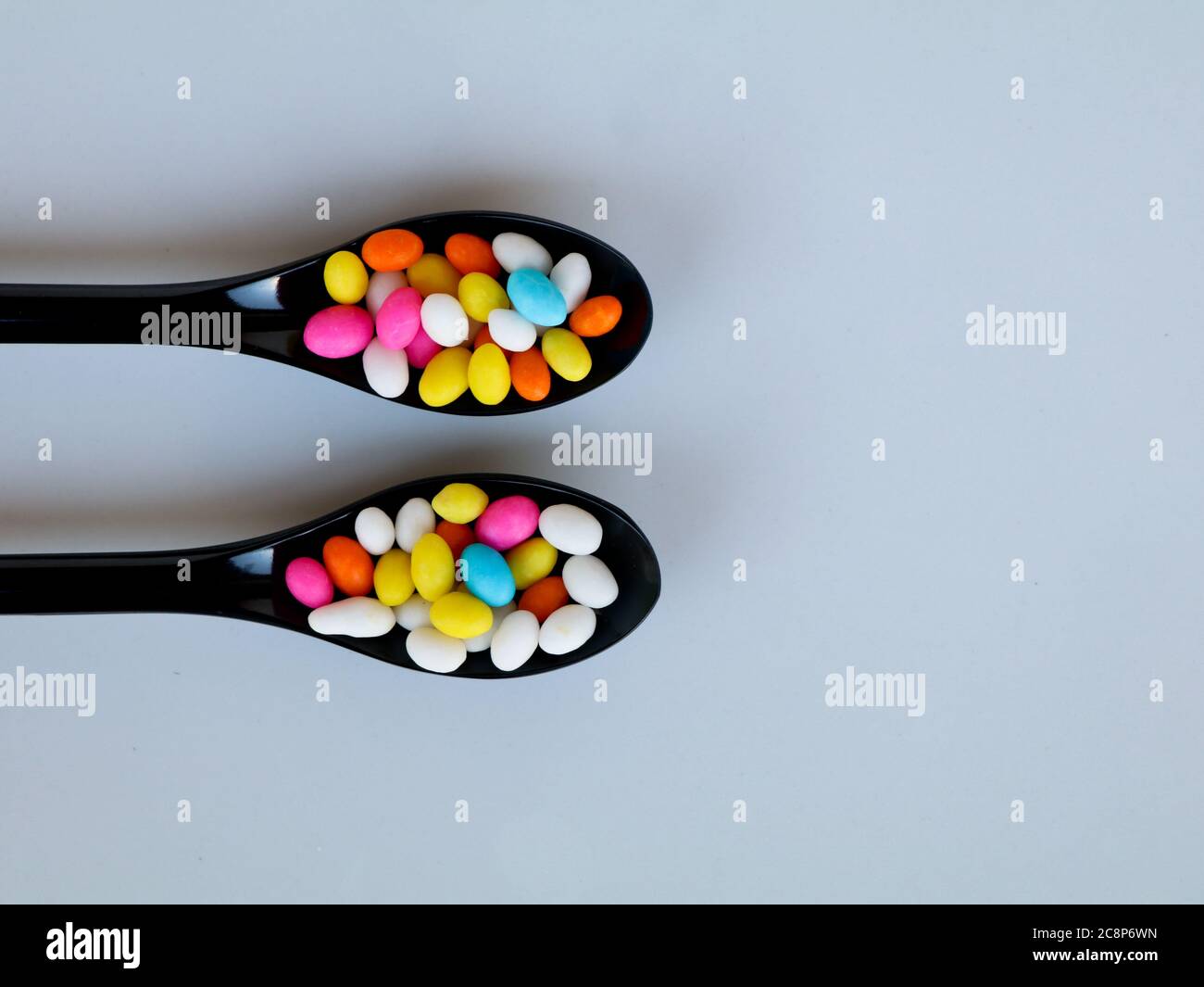 Multi colored sweet fennel sugar candy in black spoons against white