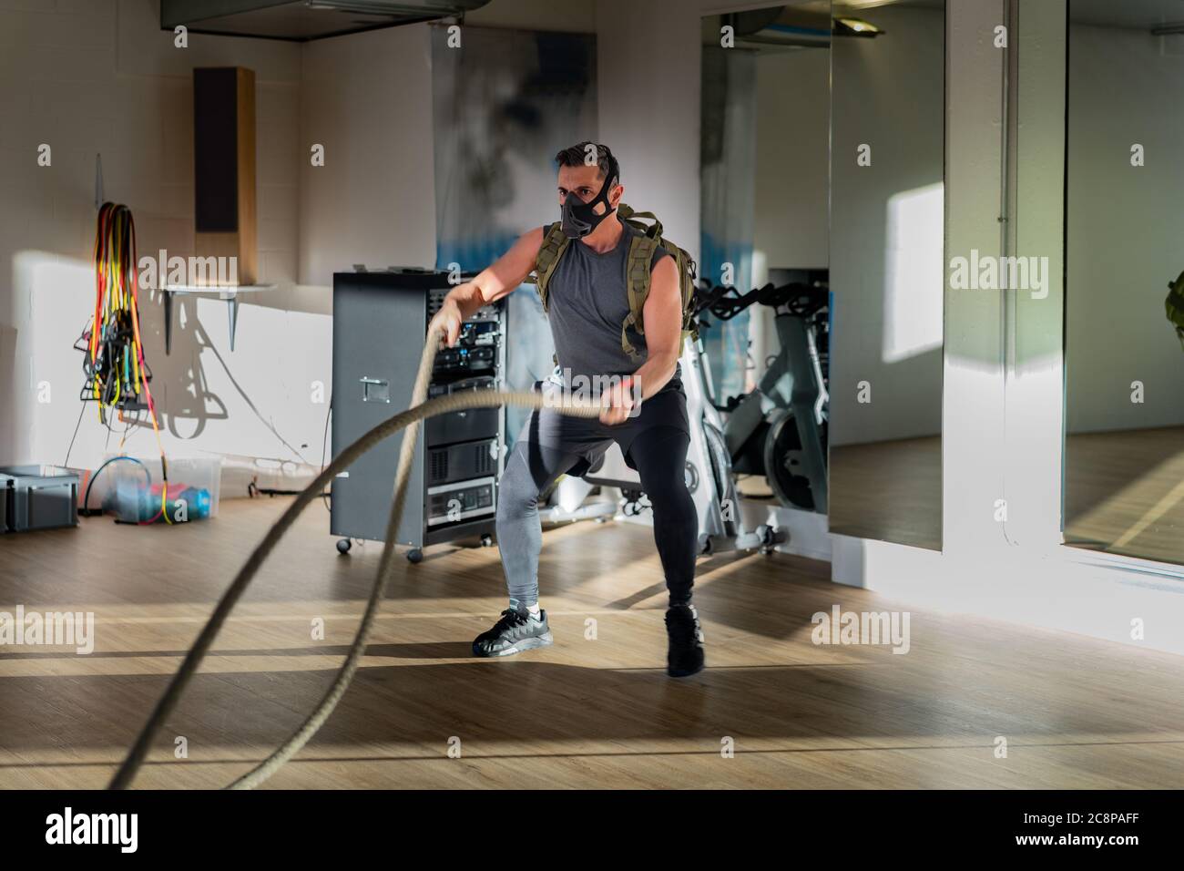 Sportsman at rope workout with training mask. Indoor on oak floor with sun and shadow. For boot camp concept. Stock Photo