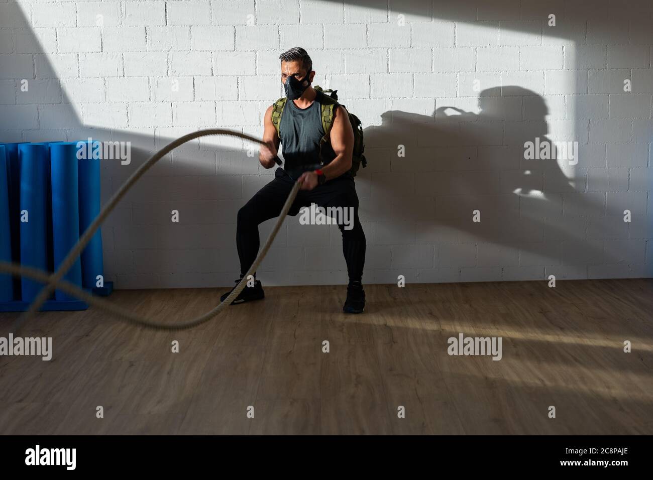 Sportsman at rope workout with training mask. Indoor on oak floor with sun and shadow. For boot camp concept. Stock Photo