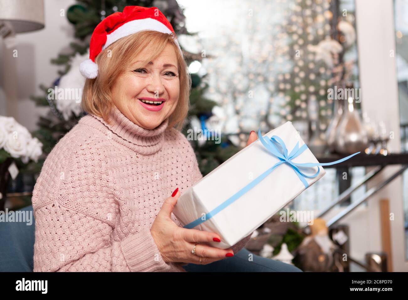 Cheerful senior woman wearing Santa Claus hat laughing to the camera ...