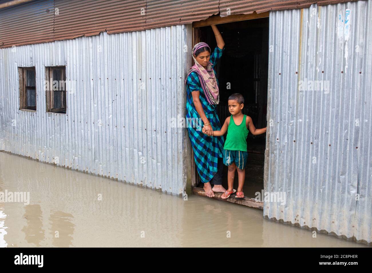A woman standing with her child on the door of her flood waded house Stock Photo