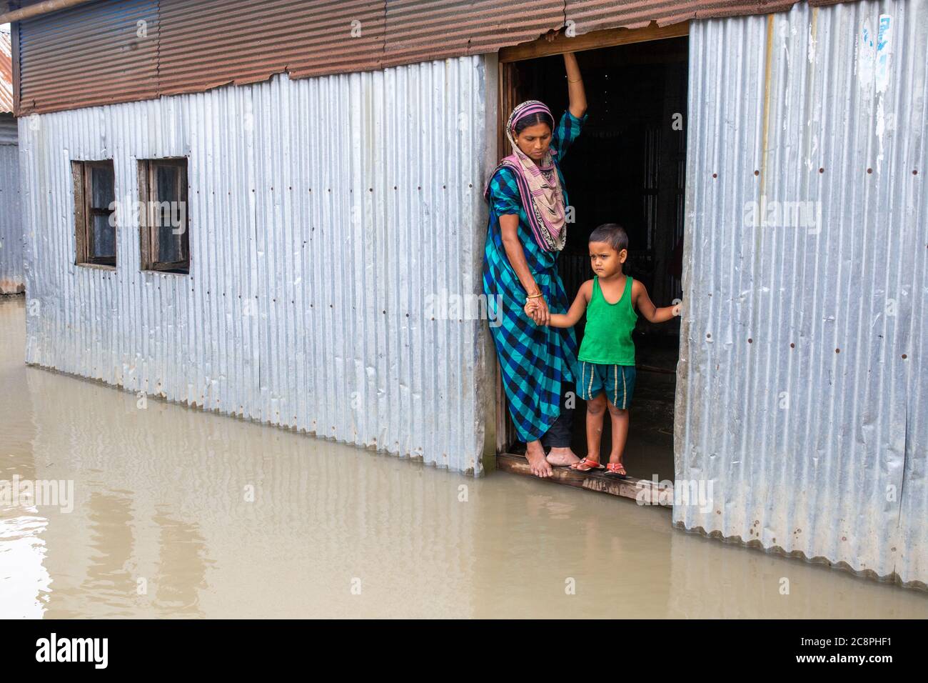 A woman standing with her child on the door of her flood waded house Stock Photo