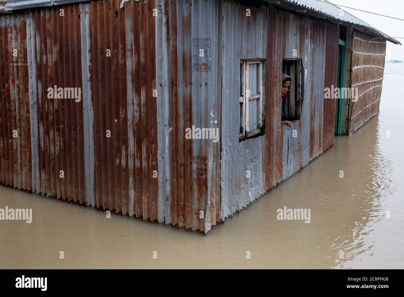 A woman looks out from the window of her flood submerged house Stock Photo