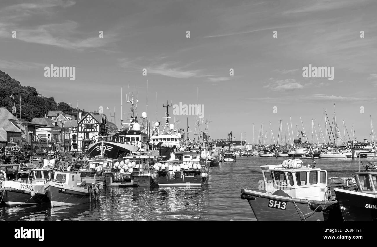 Fishing boats are moored together alongside a wharf and buildings stand along the waterfront. An ancient wall runs along the top of a hill. Stock Photo
