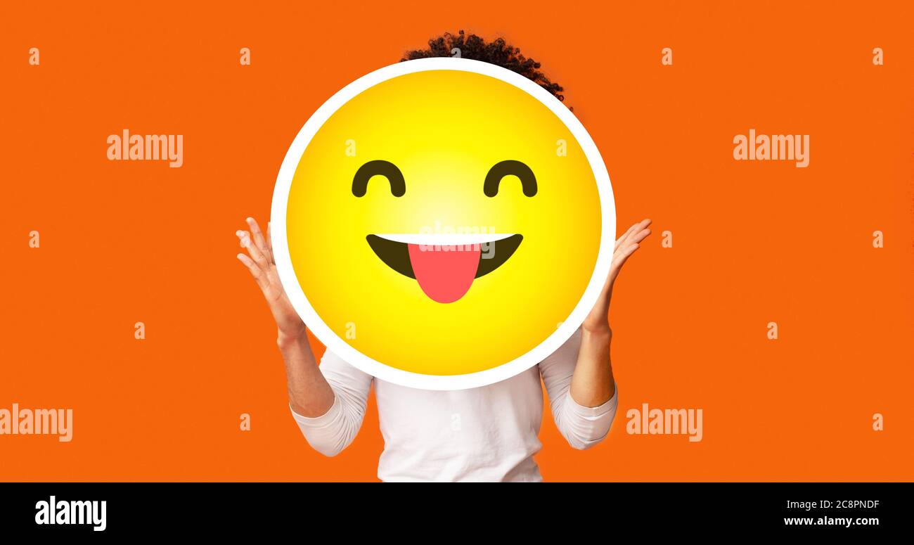 Black bushy man holding happy cheeky emoji emoticon in front of head Stock Photo