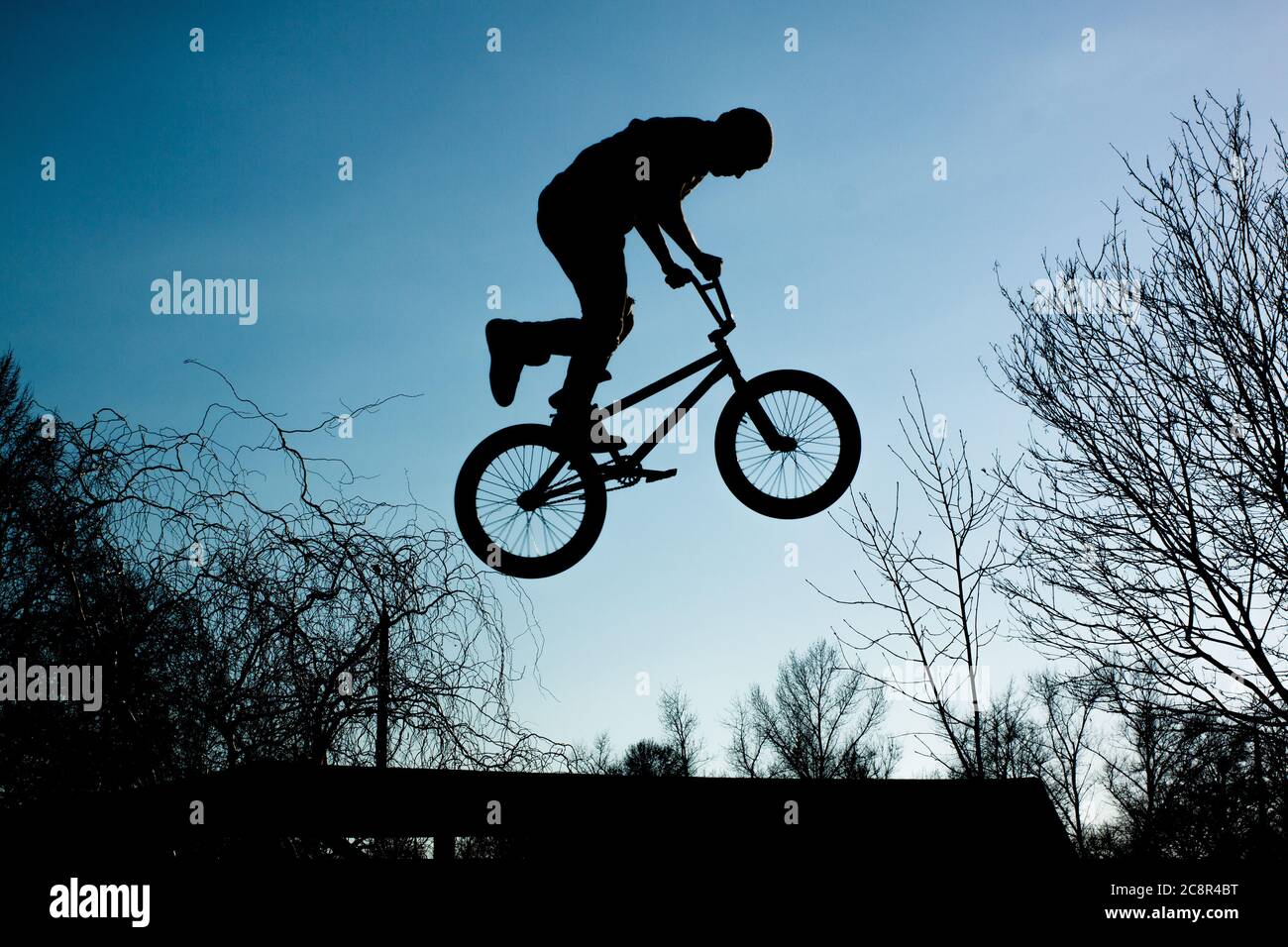 Silhouette of a man jumping on a bicycle against a blue sky with white