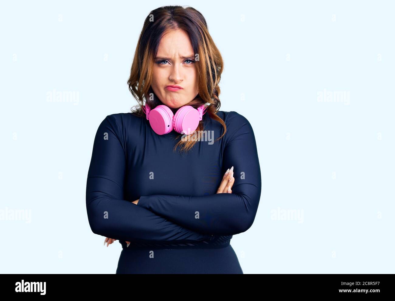 Young beautiful caucasian woman wearing gym clothes and using headphones skeptic and nervous, disapproving expression on face with crossed arms. negat Stock Photo