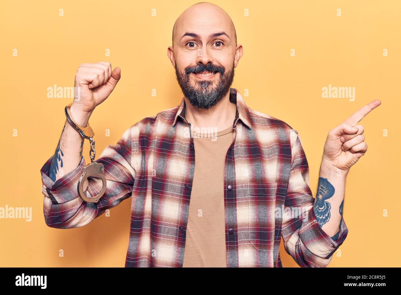 Young handsome man wearing prisoner handcuffs smiling happy pointing ...