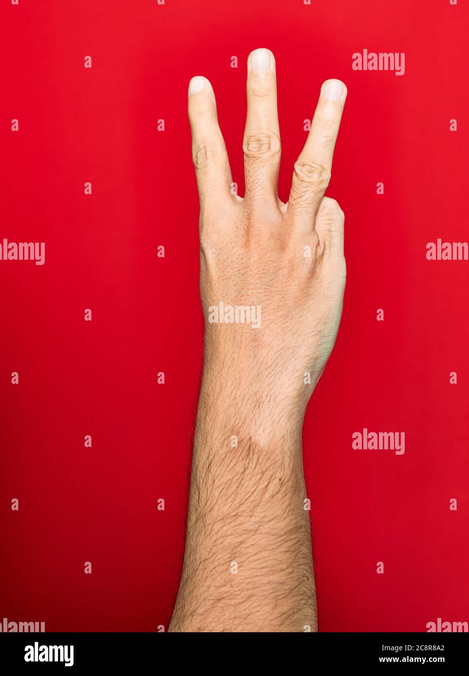 Beautiful hand of man raised up with three fingers over isolated red