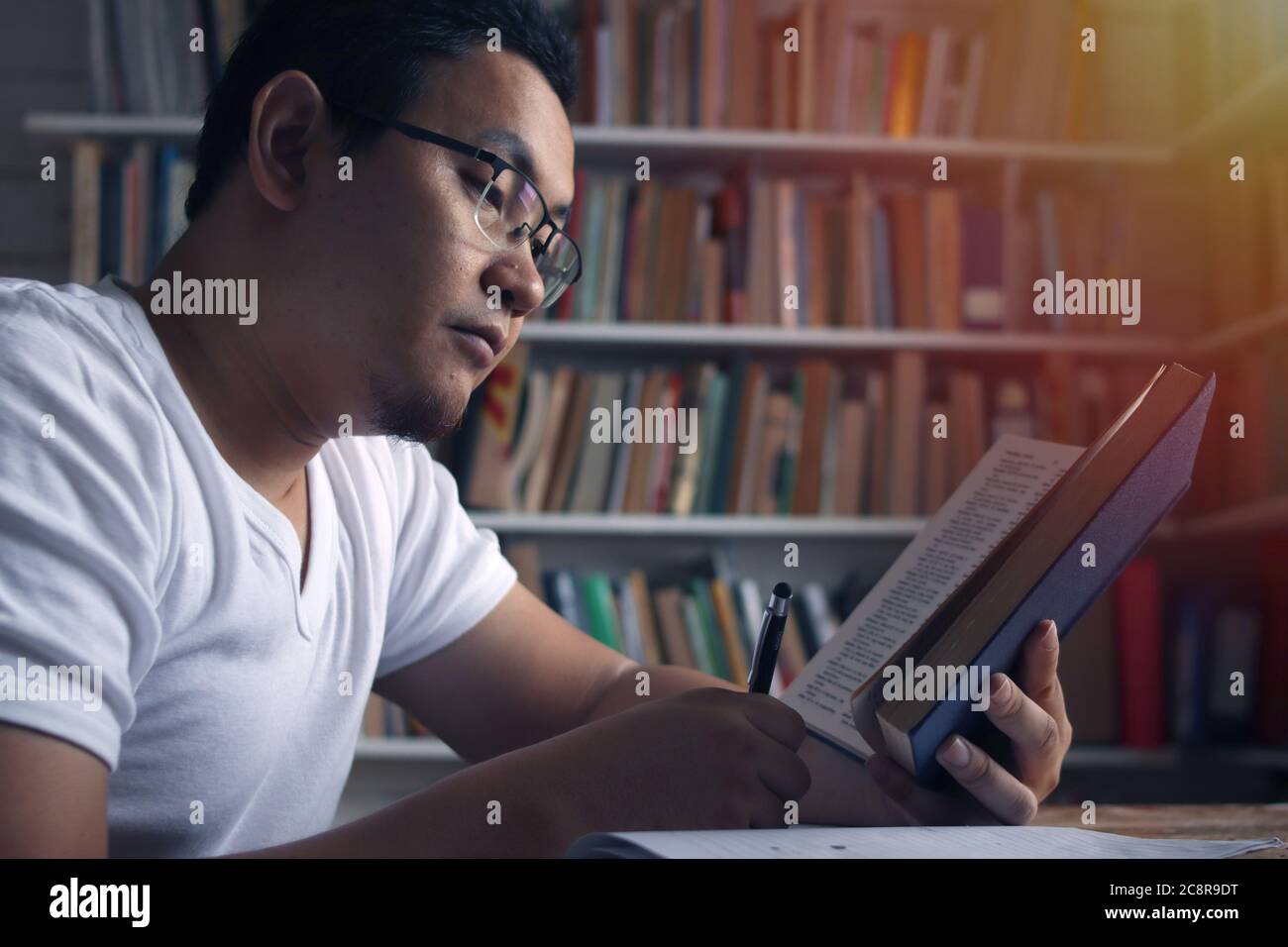 Young Asian man studying learning in library, exam preparation concept. Male college student doing research and making notes in his book Stock Photo
