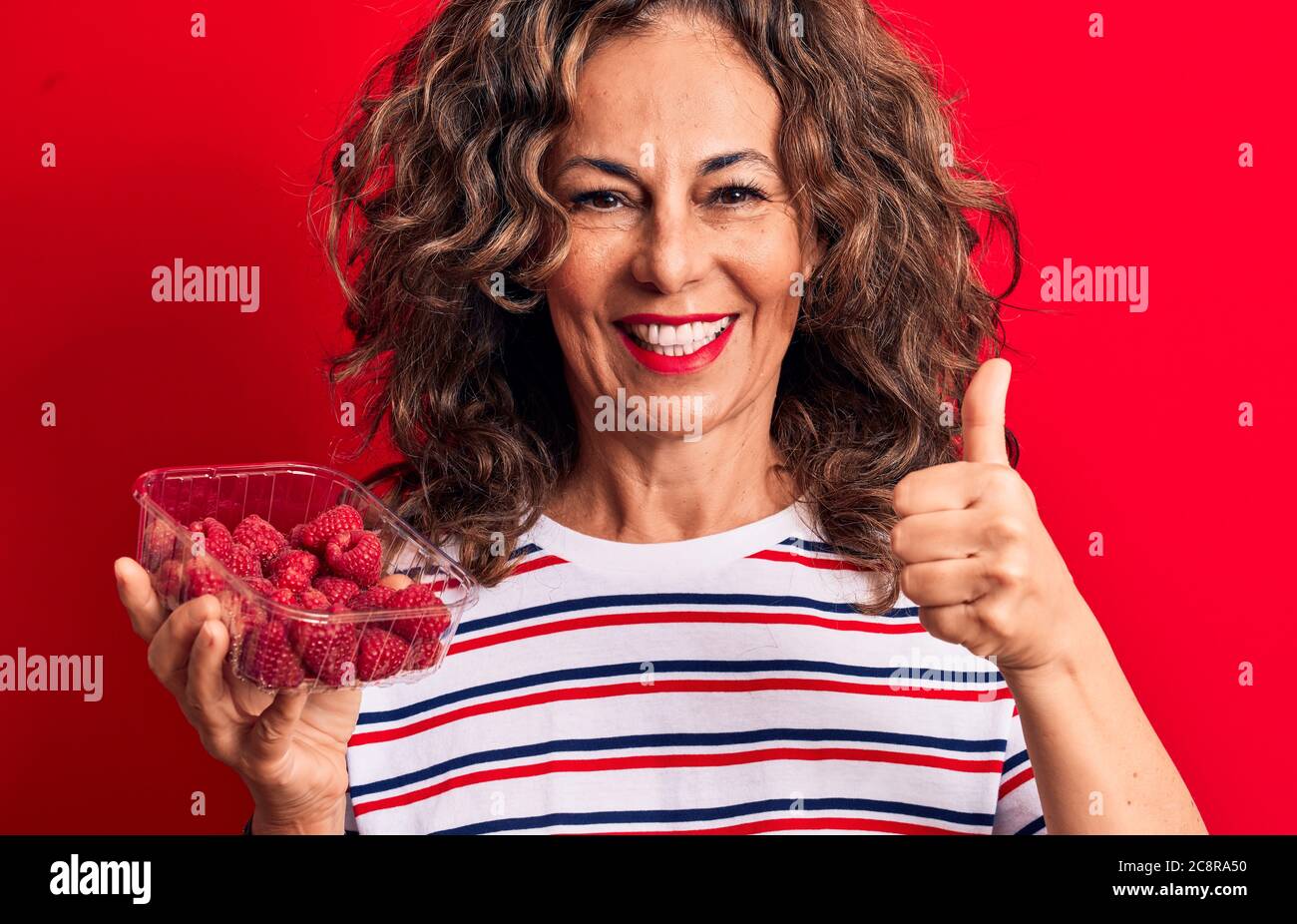 Middle age brunette woman holding box of healthy raspberries over ...