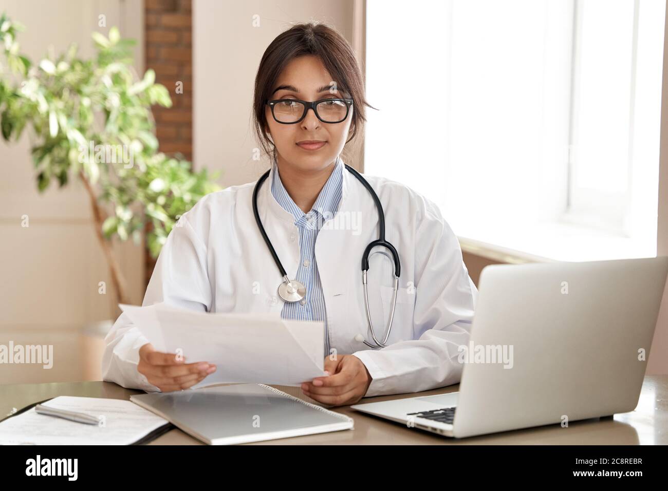 Confident indian female doctor wear white coat looking at camera at