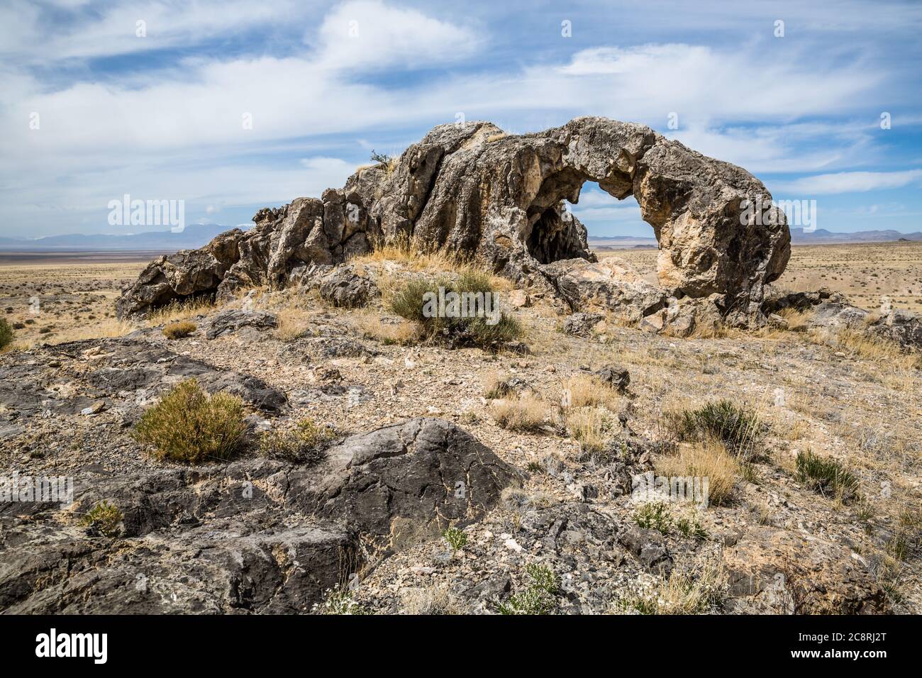 A large limestone rock formation with an unnamed arch standing over the wide open empty Utah desert. Stock Photo
