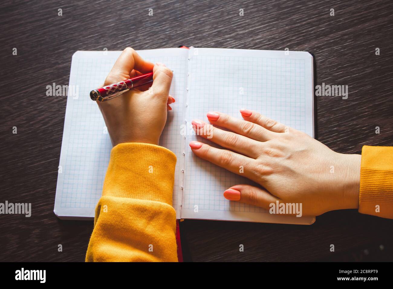 Young woman holds a pen in her left hand and writes a note in blank
