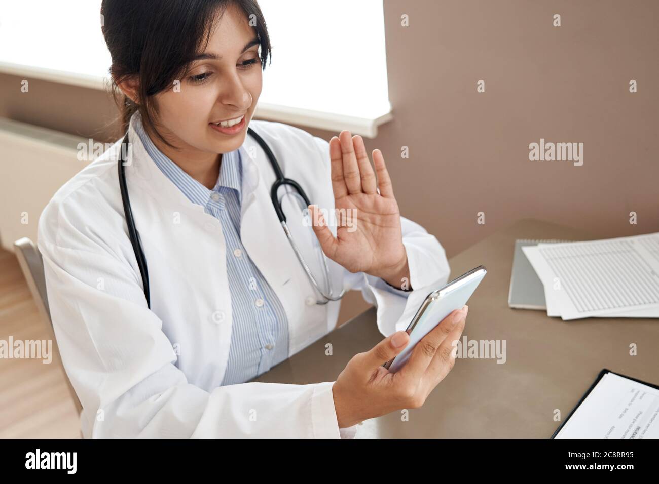 Indian female doctor video calling patient in online mobile phone app. Stock Photo