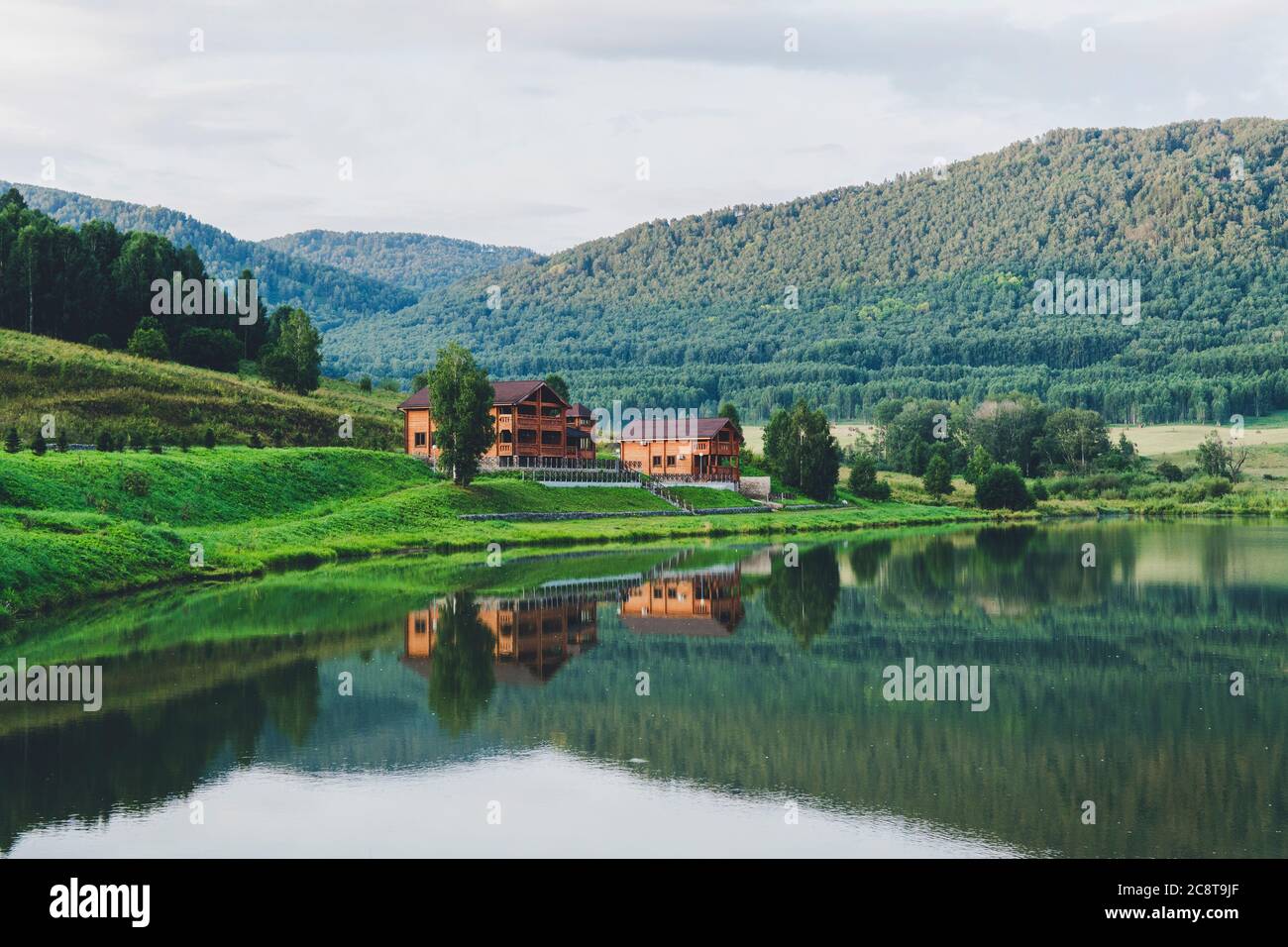 Beautiful landscape of mountains and lakes. The log house is reflected in the clear water. Tourist base in mountains. Country house for Stock Photo