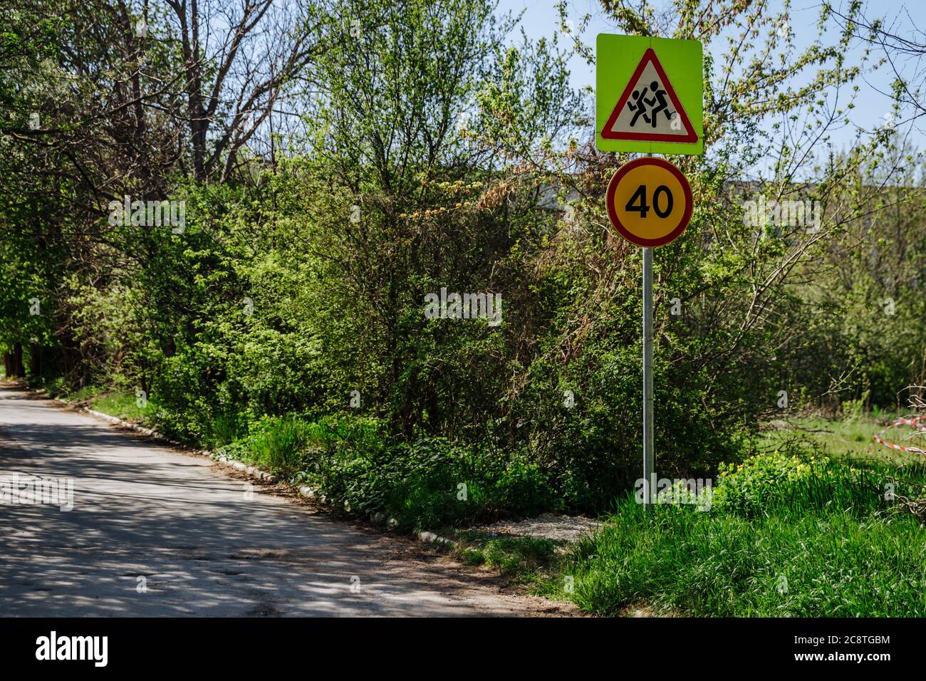 Two road signs on one pillar caution children sign and speed limit sign 40. Signs on the background of branches and blue sky on the street on a sunny day. Stock Photo