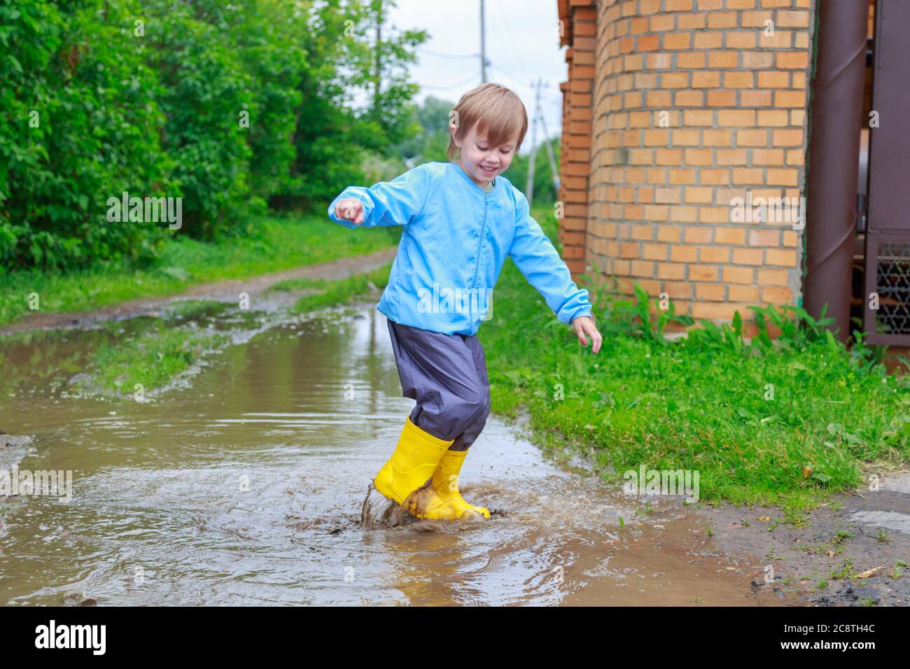 .Child in rubber boots and raincoat playing in a puddle Stock Photo - Alamy