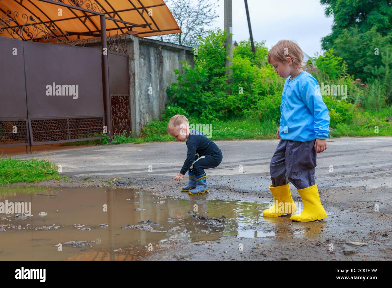 .children in rubber boots and raincoats play in a puddle Stock Photo ...