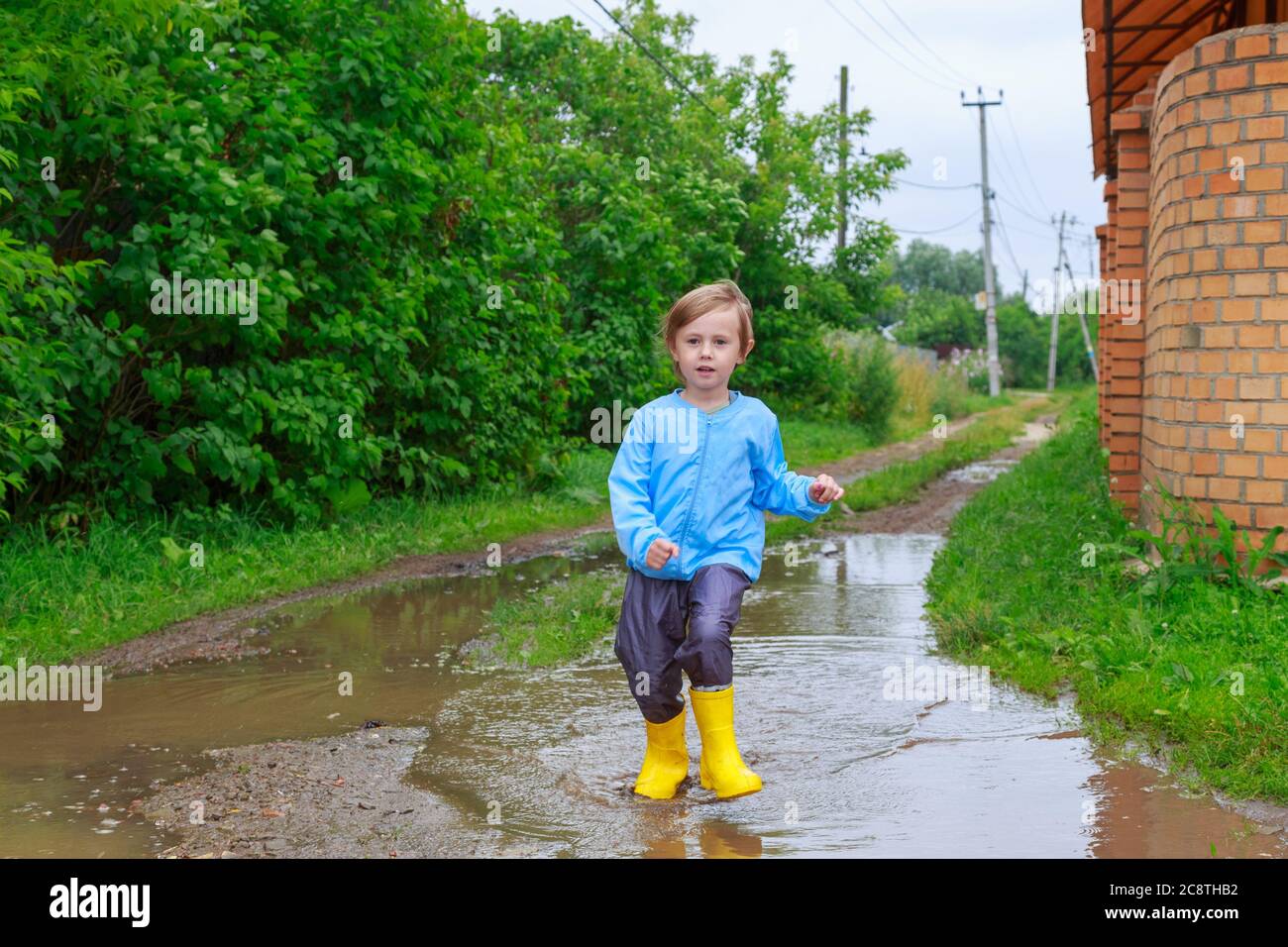 .Child in rubber boots and raincoat running in a puddle Stock Photo - Alamy
