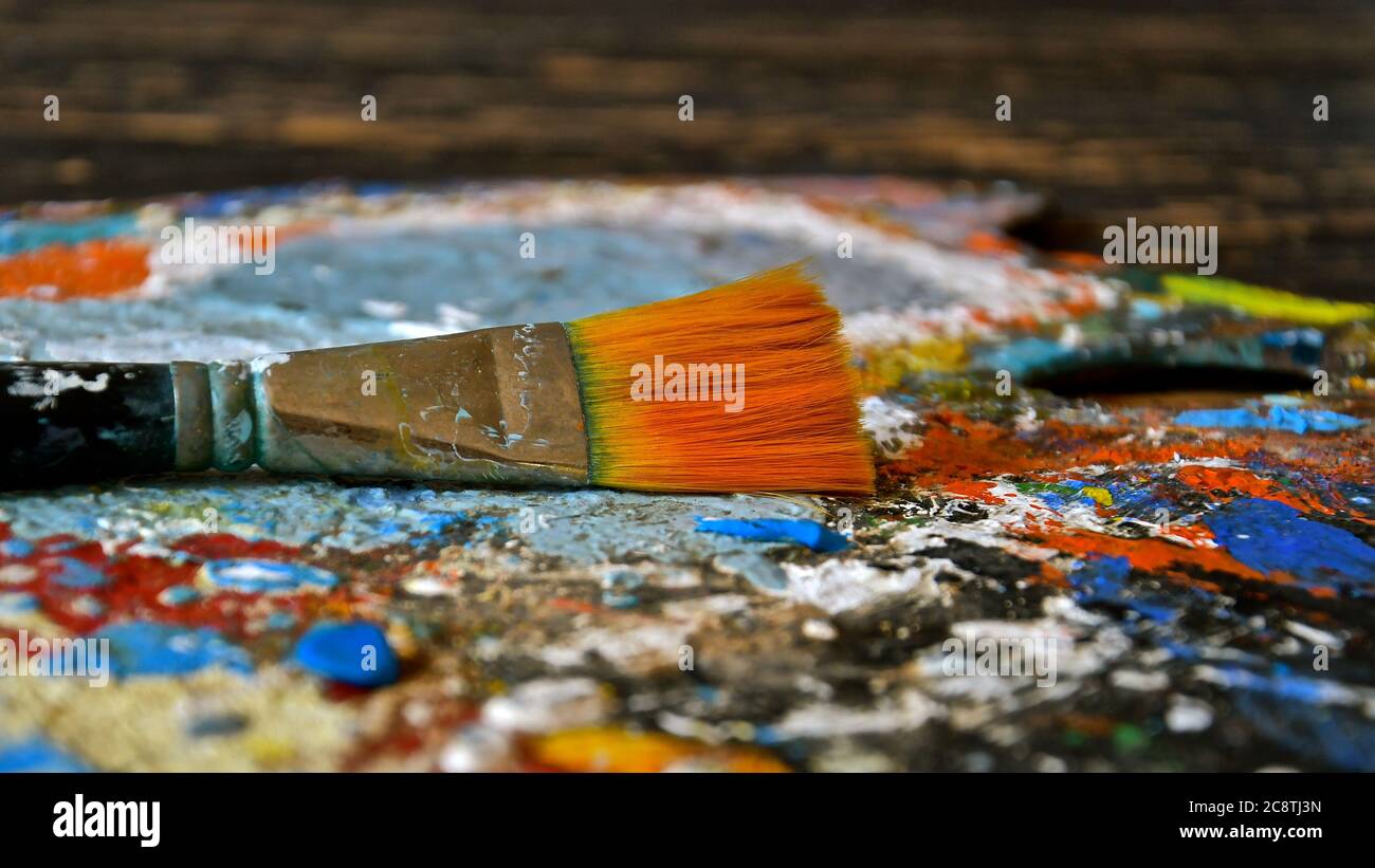 Side profile view of a paint brush resting on a paint splattered textured painting palette. Stock Photo