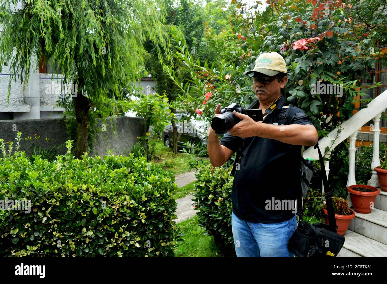 An Indian man wearing cap and glasses taking picture with camera in a garden, selective focusing Stock Photo