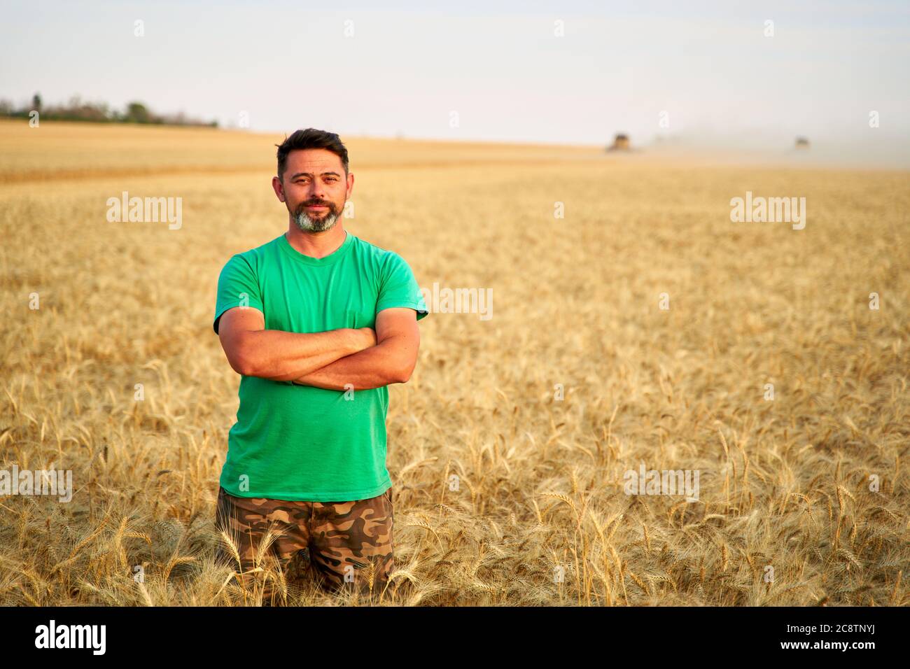 Happy farmer proudly standing in wheat field with arms crossed on chest ...