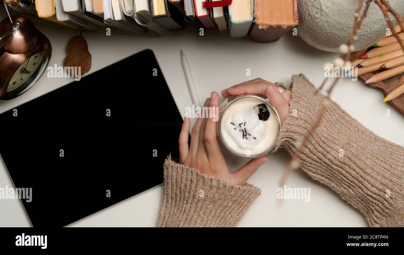 Overhead shot of female hands holding a cup of beverage on worktable ...