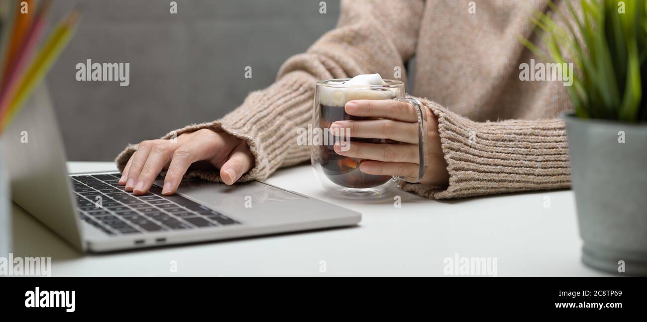 Side view of female working with laptop and holding a cup of beverage ...