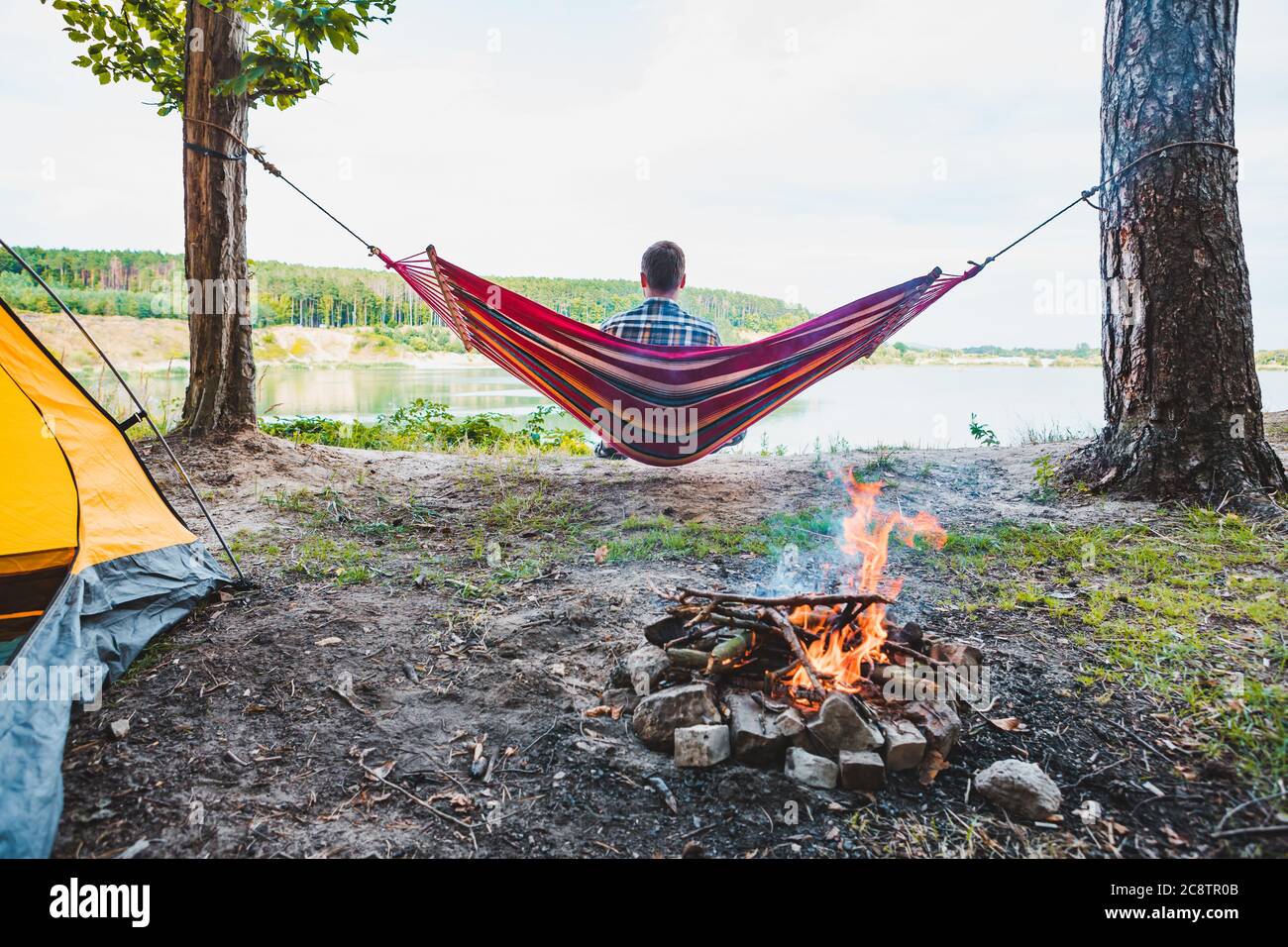 man laying on hammock at lake beach near camp fire Stock Photo Alamy