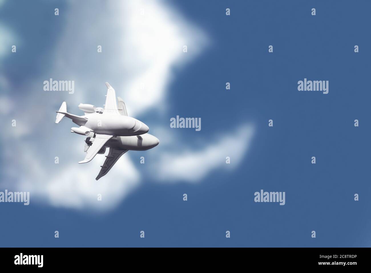 A white toy plane stands on a mirror that reflects a blue sky with clouds. Stock Photo