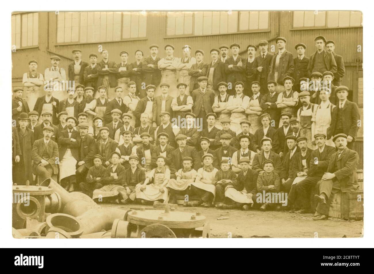 Original early 1900's Edwardian era postcard of men and boy workers in a yard, all wearing flat caps, overalls, could be a foundry casting pipes, some of the men could be pattern makers, posted from Exeter in Devon, June 1907, U.K. Stock Photo