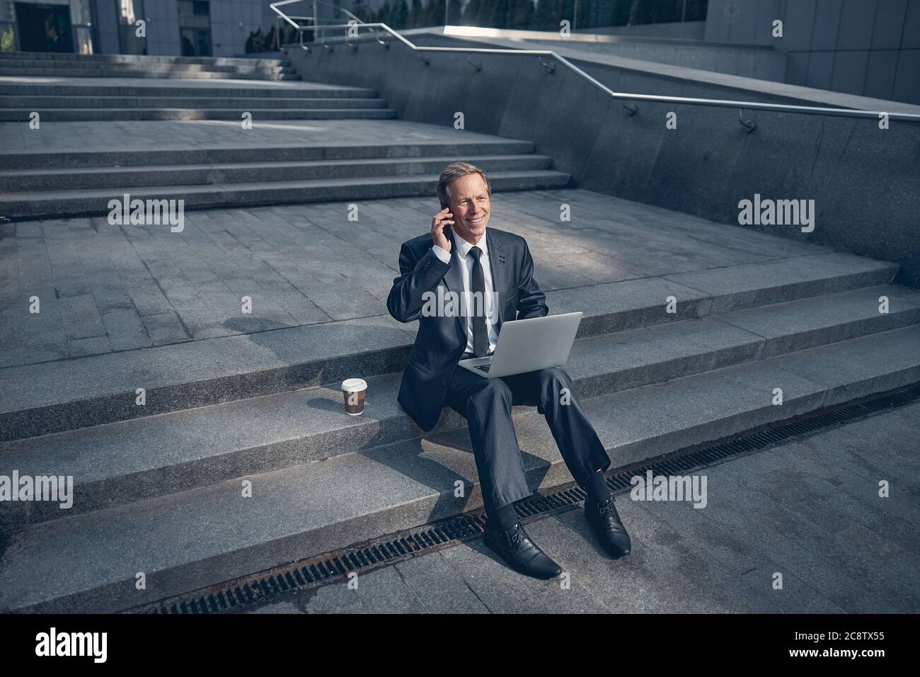 Joyful man using laptop and talking on cellphone outdoors Stock Photo