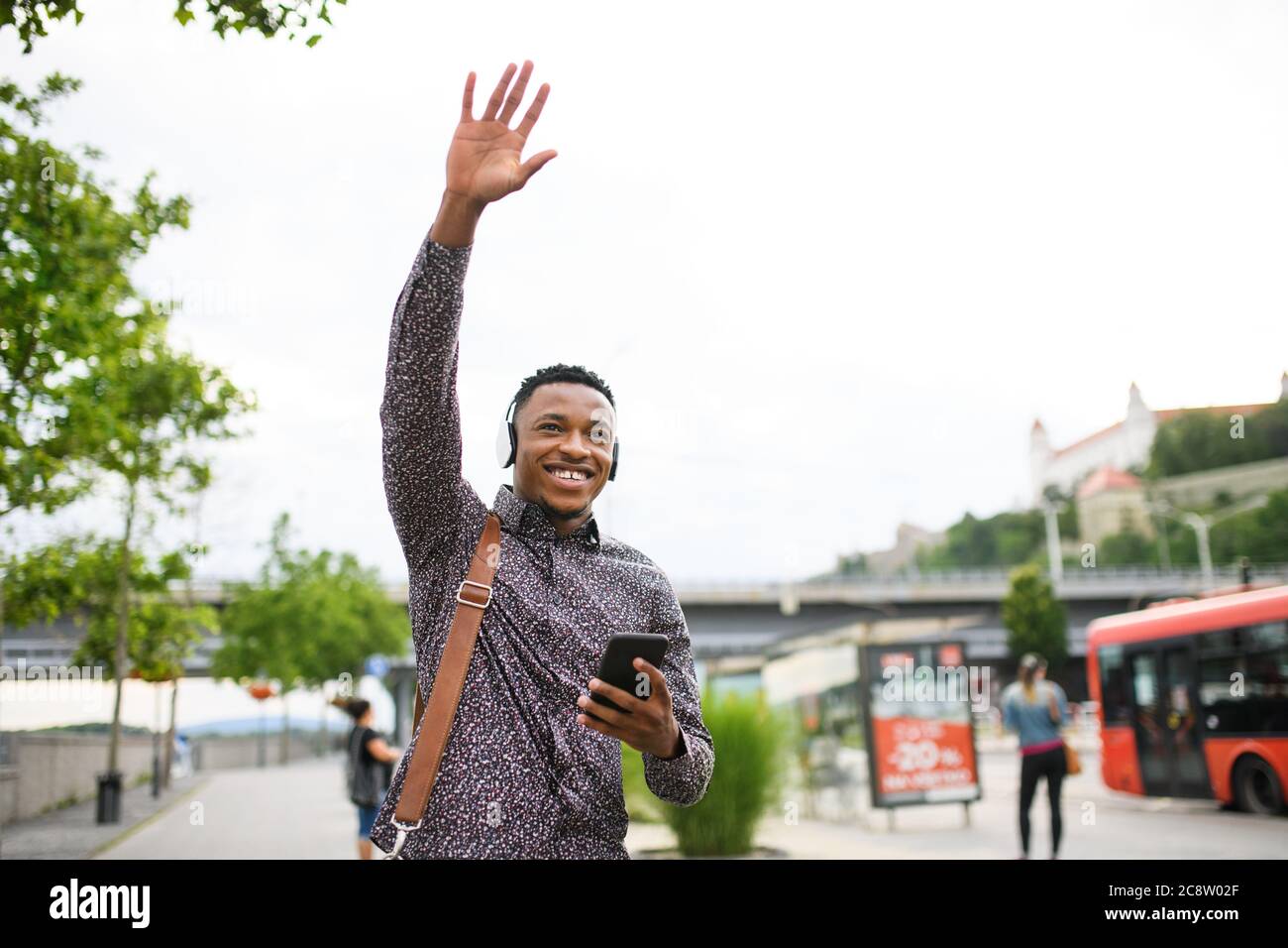 Cheerful young black man commuter outdoors in city, greeting somebody. Stock Photo