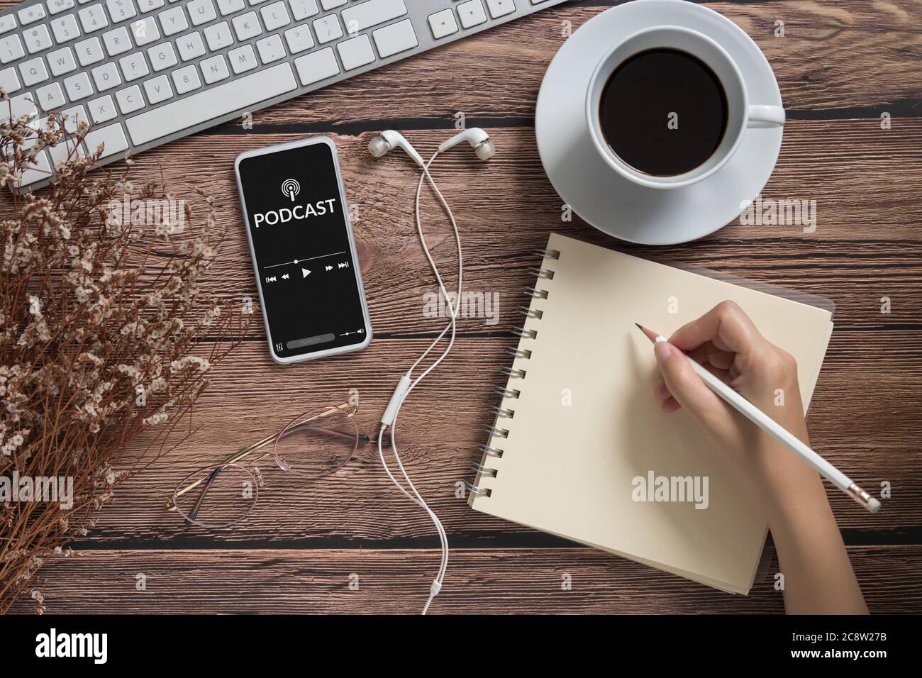 podcast audio content concept. podcast application on mobile smartphone screen on wooden table with coffee cup, earphones, glasses, notebook, pencil Stock Photo