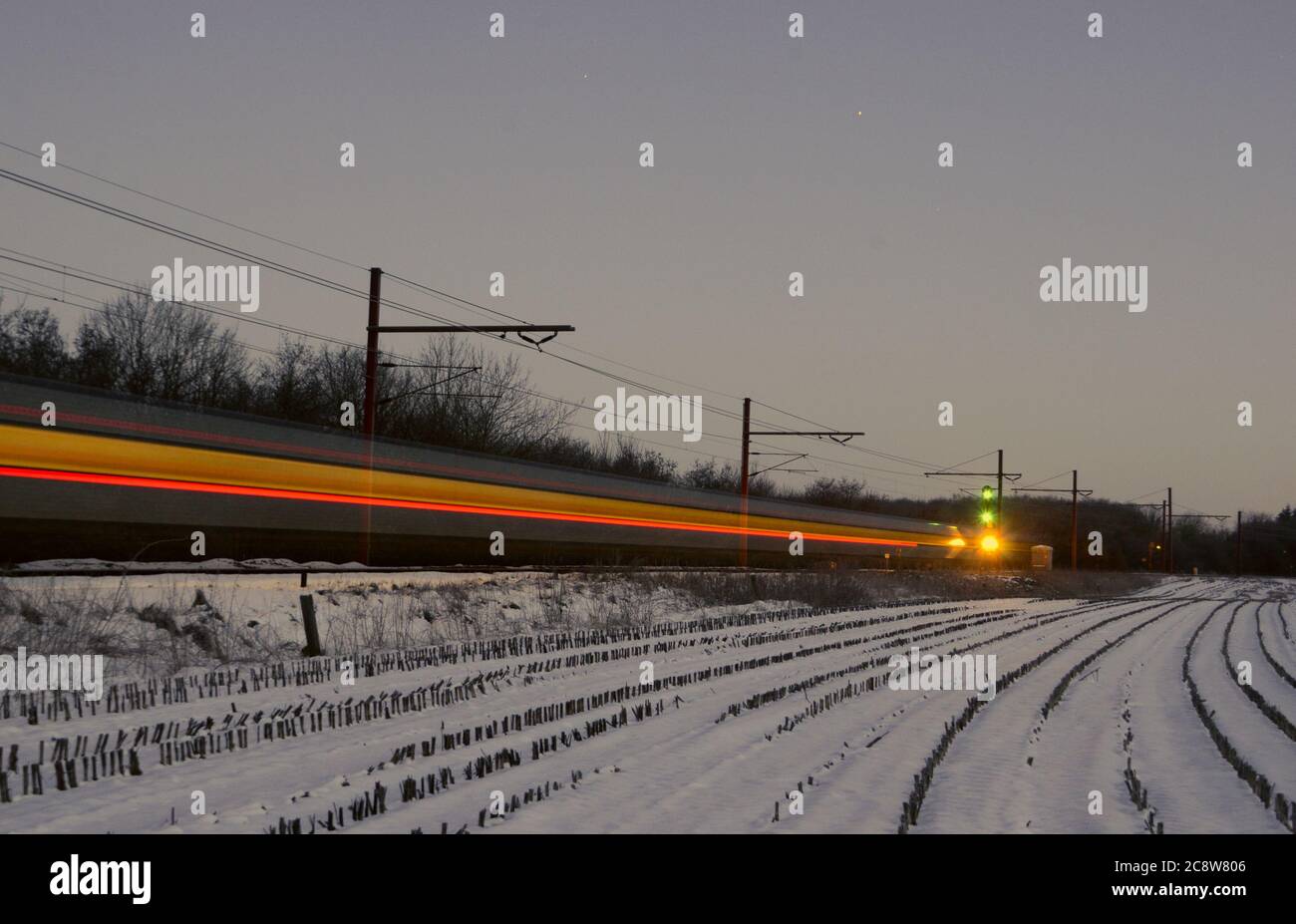 In the 'blue hour' during dawn of a cold winter's day, an international train passes Tinglev in Denmark, leaving light trails during the long time exp Stock Photo