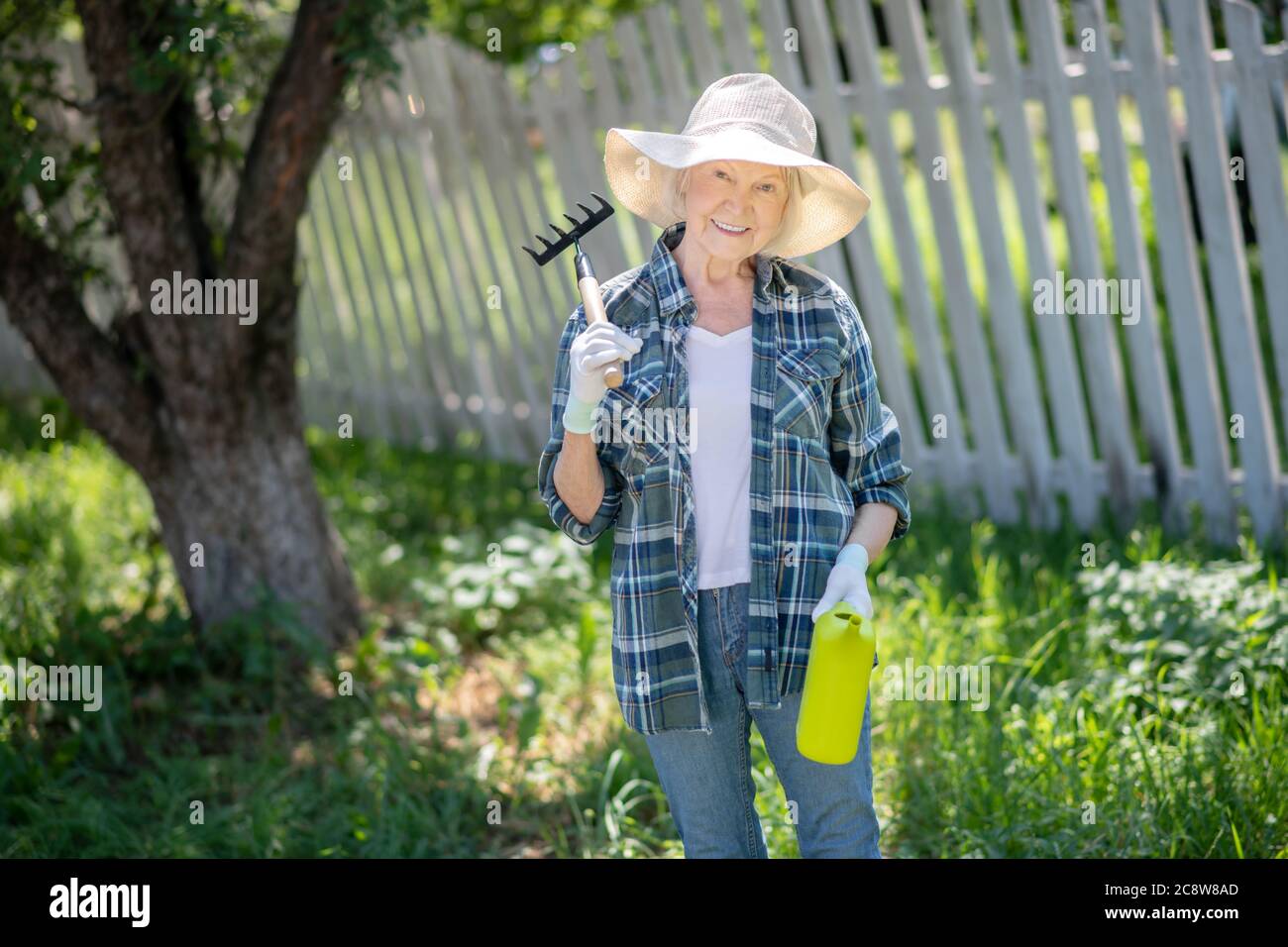 Woman holding a rake and a watering can Stock Photo - Alamy