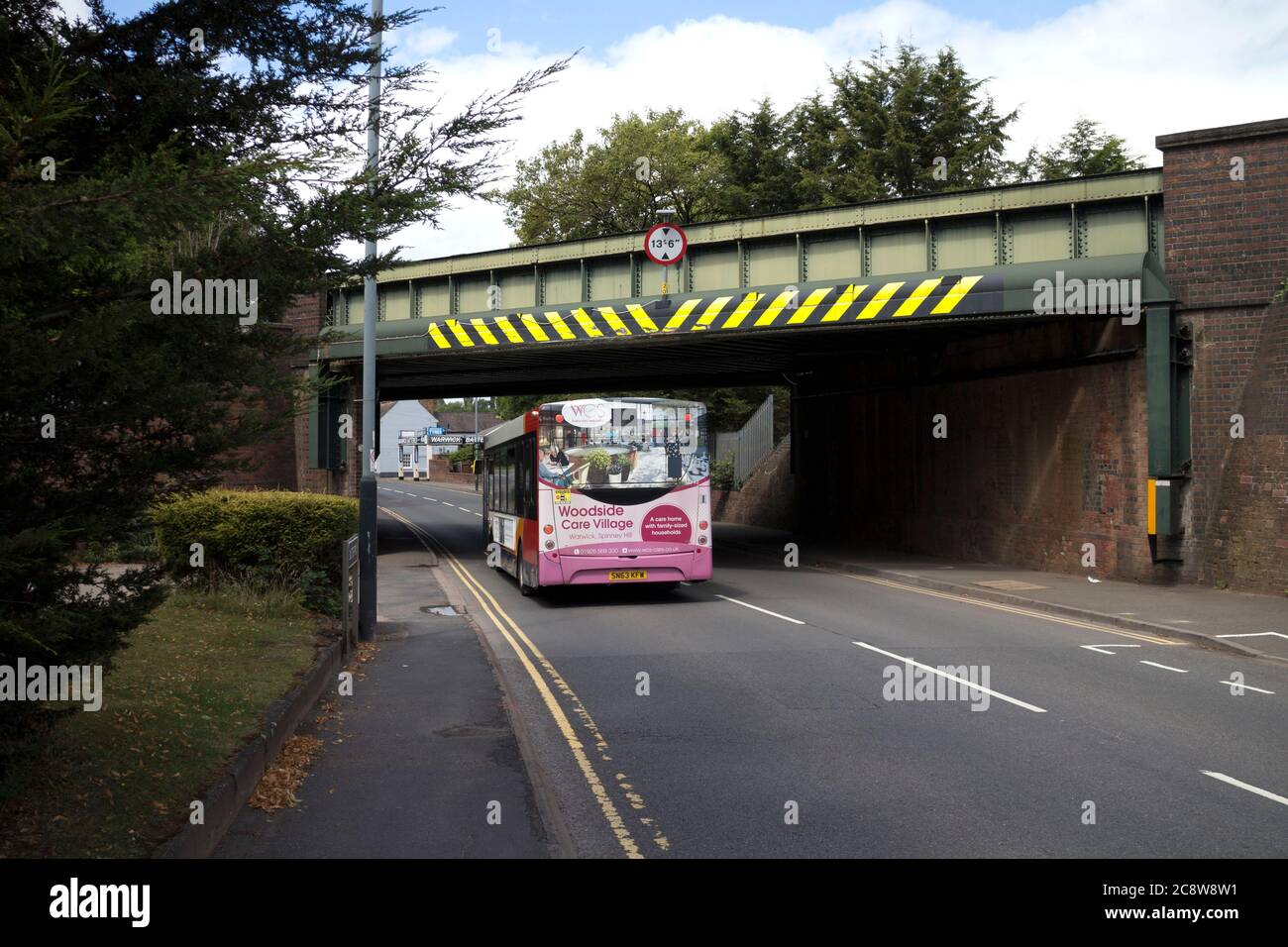 A single-decker bus going under a metal railway bridge in Birmingham Road, Warwick, Warwickshire, England, UK Stock Photo