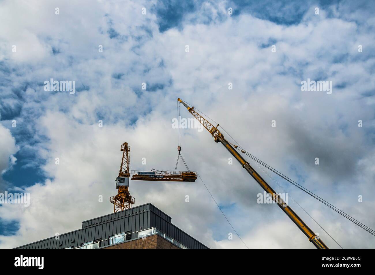 Mobile crane taking down tower crane during apartment construction in