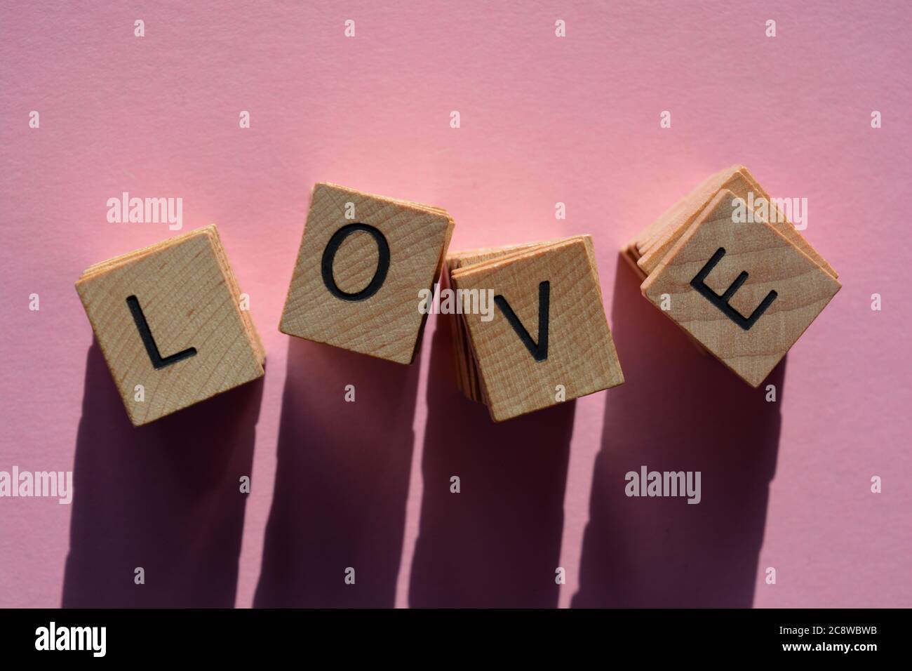 Love, word in stacks of 3d wooden alphabet letters isolated on pink