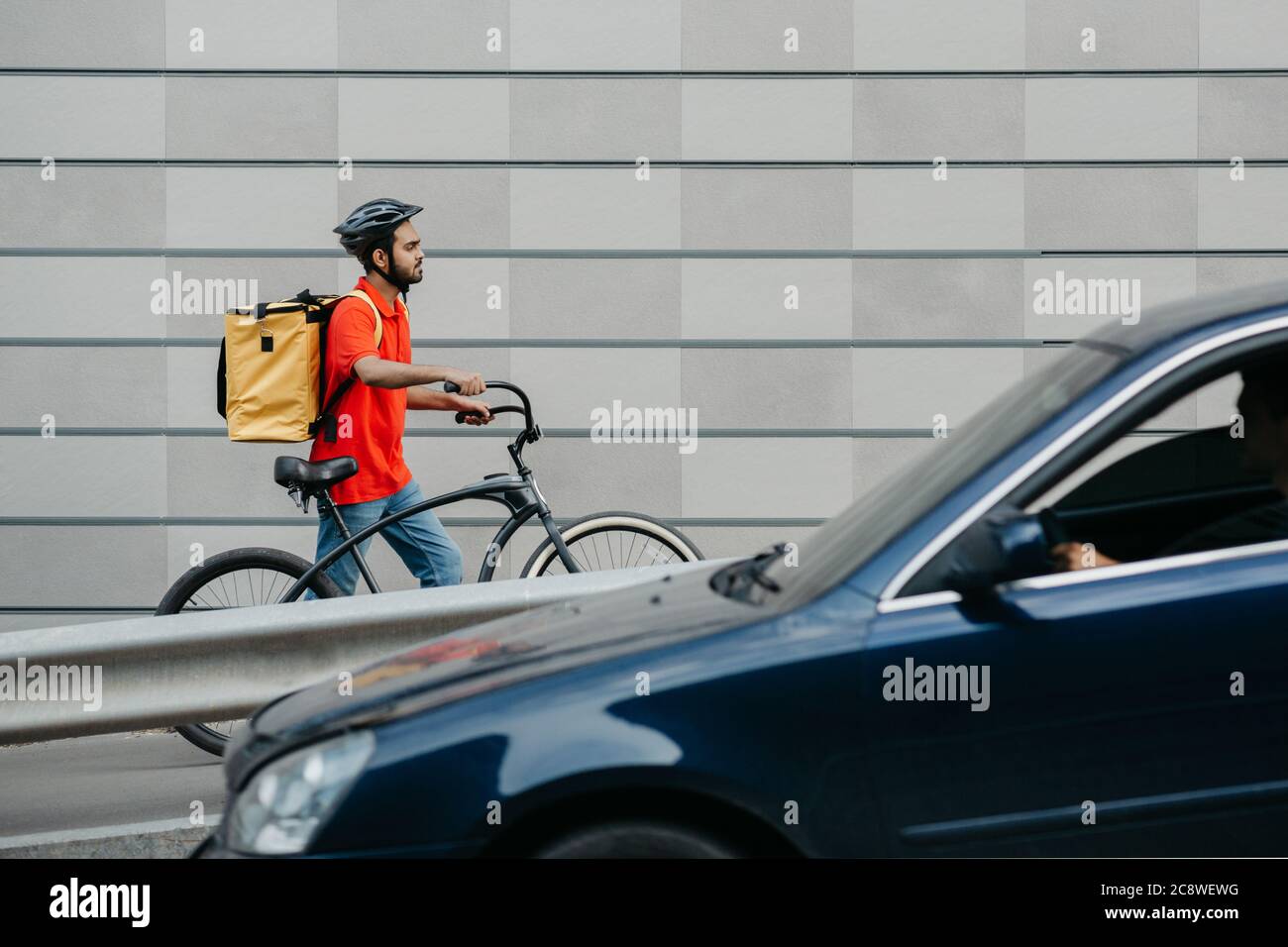 Delivery by courier in city. Guy in helmet and with backpack, going through city with bicycle Stock Photo