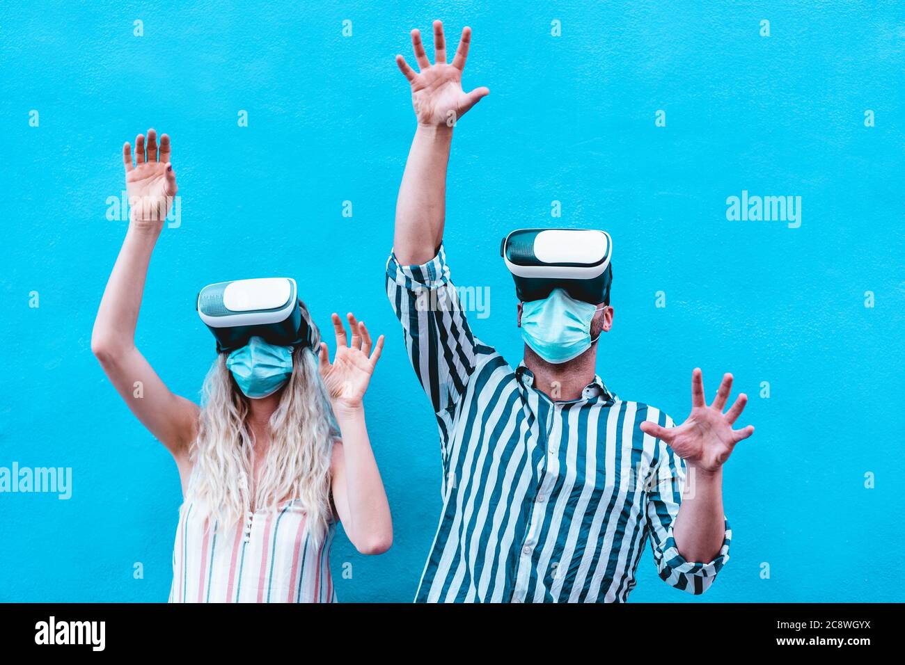 Young people using virtual reality glasses while wearing protective face masks for coronavirus prevention - Technology and social distance lifestyle - Stock Photo