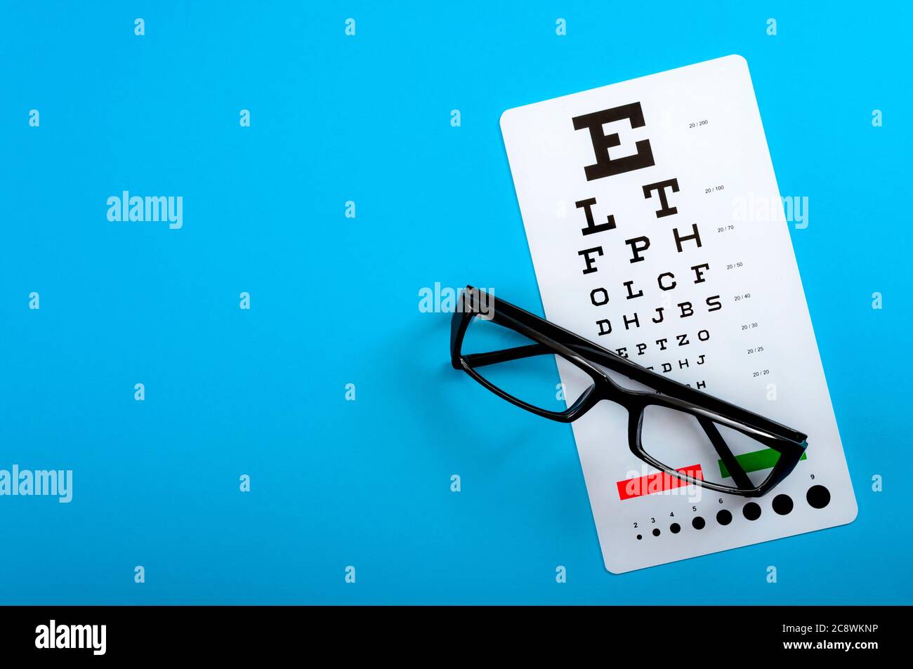 Ophthalmological exam, healthy eyes and ophthalmology concept with a pair of vision glasses and an eye chart isolated on blue background with copy spa Stock Photo