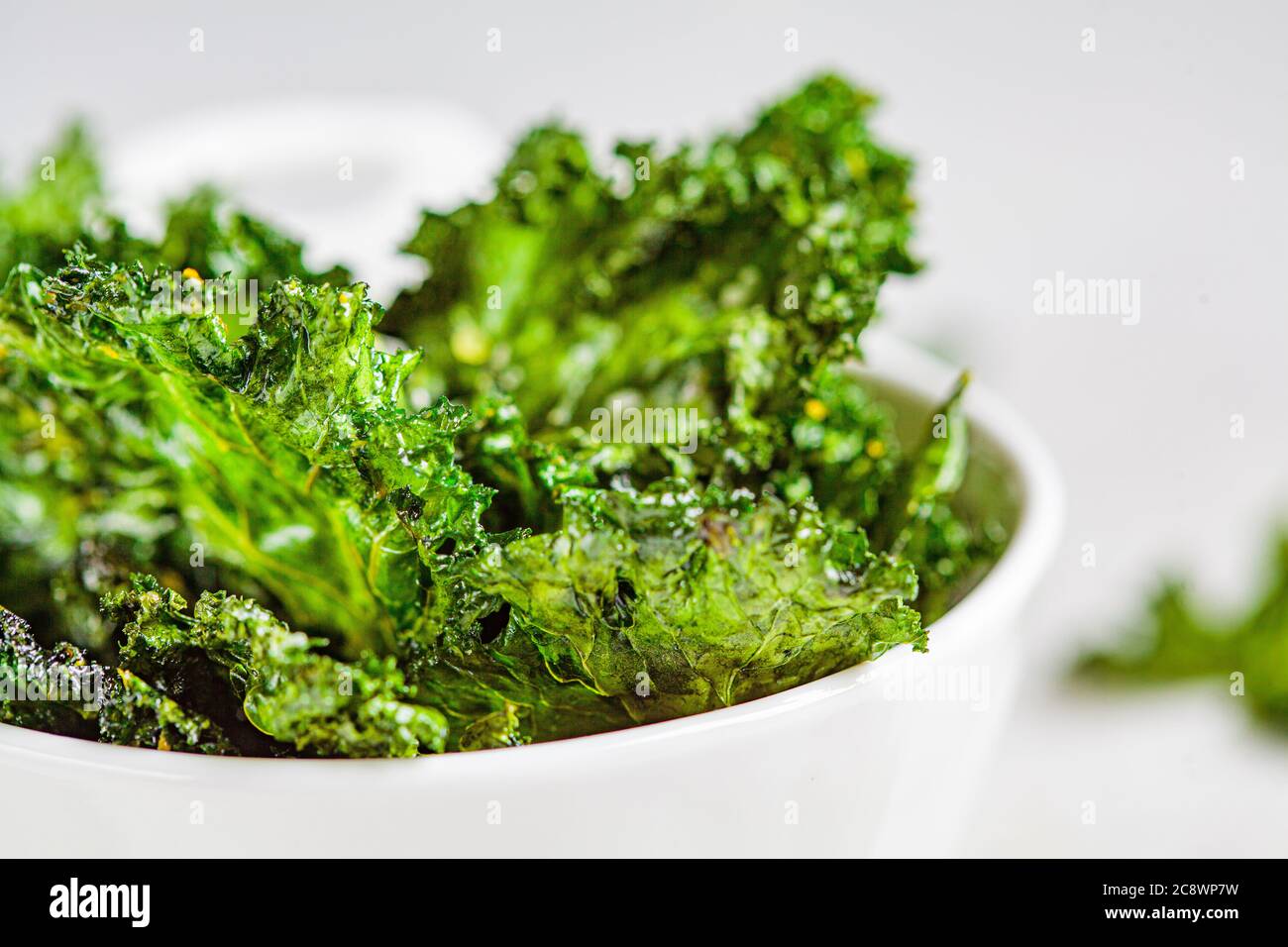 Green kale chips with salt in a white bowl. Healthy vegan food concept