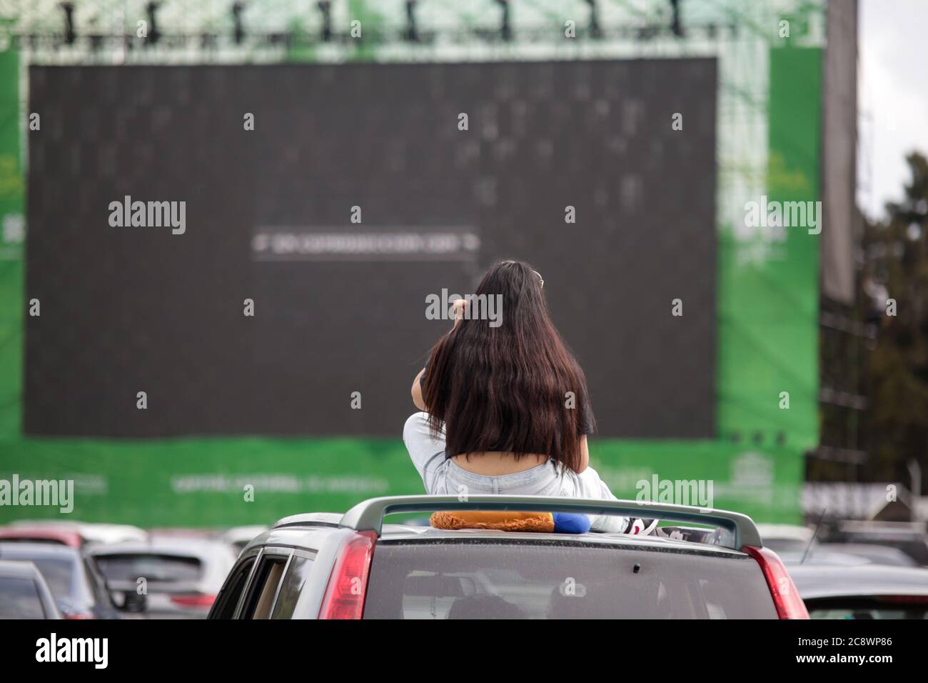 Mexico City, Mexico. 26th July, 2020. A woman sits on top of her car while watching a movie at a drive-in movie theater in Mexico City, Mexico, July 26, 2020. Drive-in movie theaters have become sought-after in Mexico during the COVID-19 pandemic. Credit: Francisco Canedo/Xinhua/Alamy Live News Stock Photo