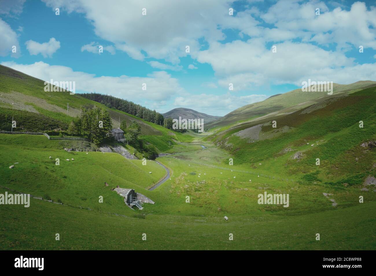 A scenic view with old scottish house, grazing sheep and a river flowing on the valley. Pentland Hills Regional park, on the outskirts of Edinburgh in summer at midday on a clear day Stock Photo