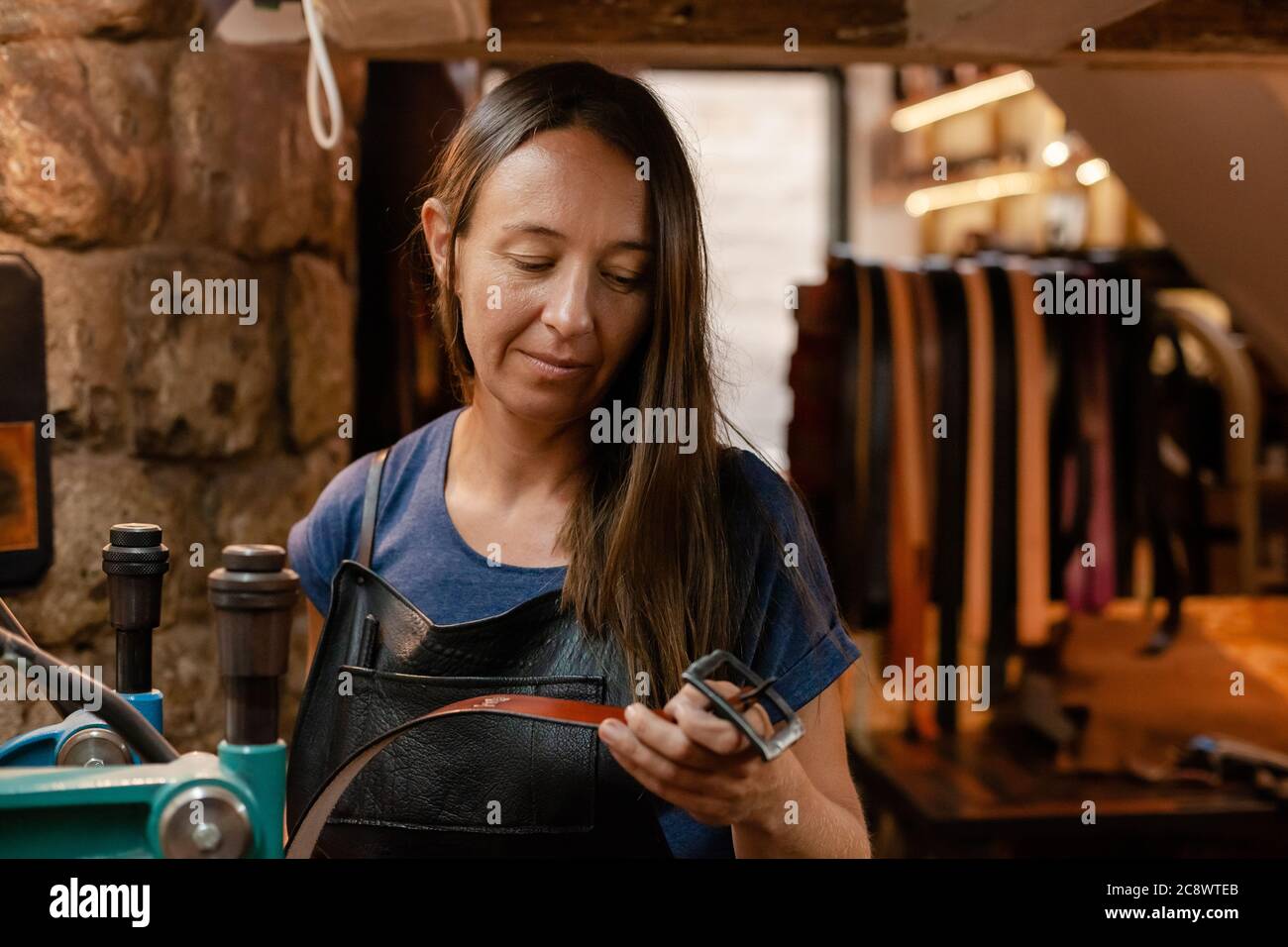 Young leather craftswoman in her traditional workshop holding a handmade belt Stock Photo